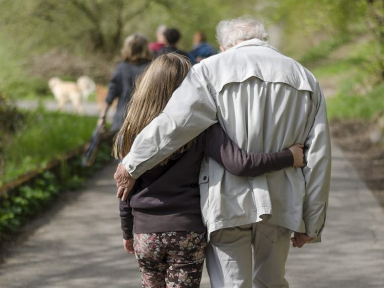 Adulto e criança caminhando de mãos dadas por um caminho arborizado.
